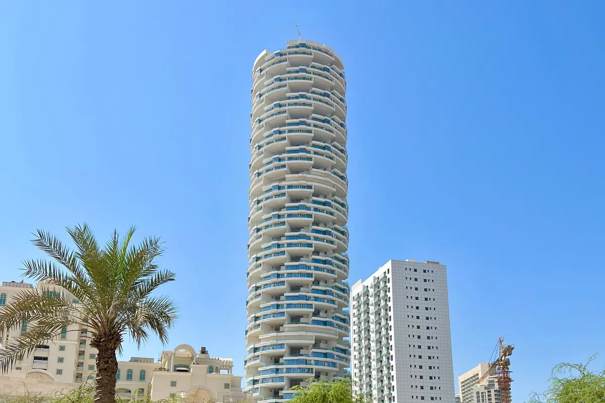 A round residential tower rising above palms and a community park in Dubai