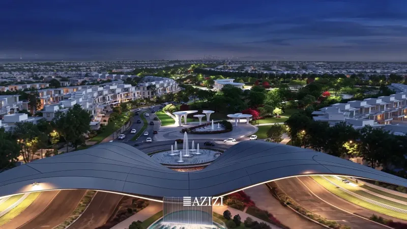 Night aerial of the illuminated central boulevard and water features at Azizi Florence, Sharjah