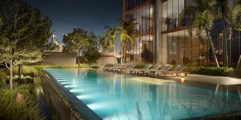 Swimming pool lined with sun loungers and trees at Burj Capital in the evening