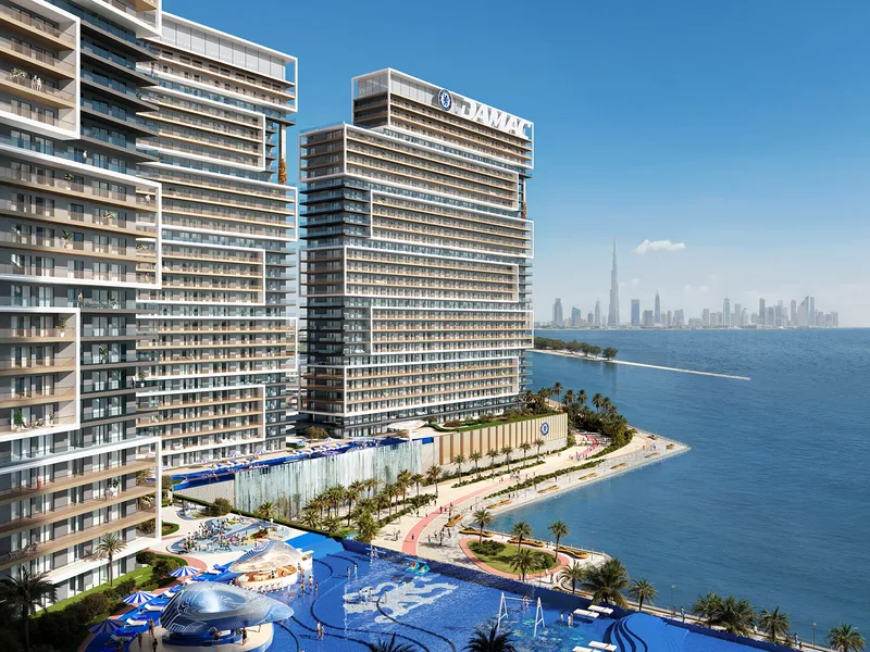 Chelsea Residences tower beside a beach and pool deck, with the Dubai skyline across the water
