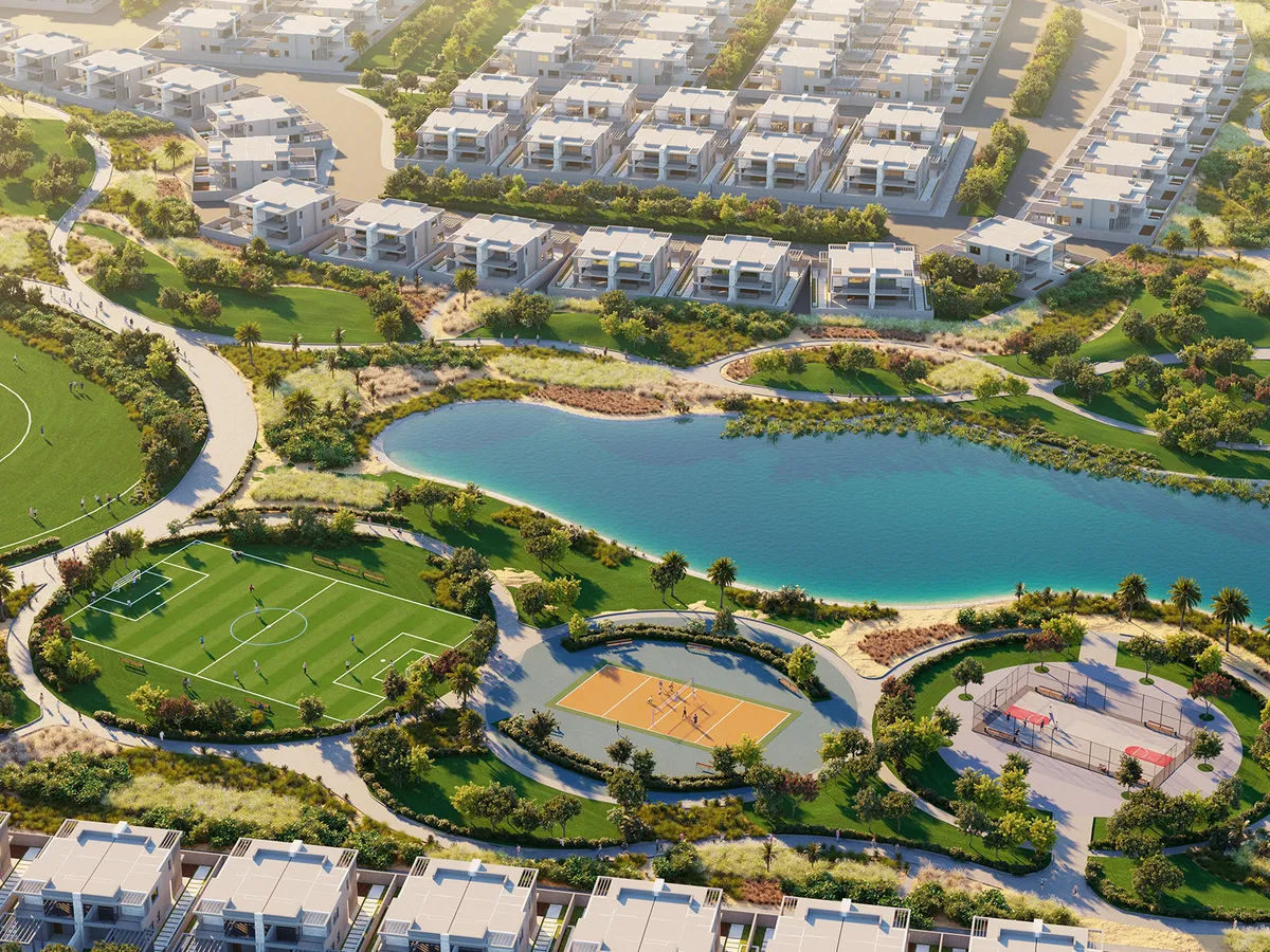 Aerial view of DAMAC Hills 2 townhouses around a lake, sports pitch and courts
