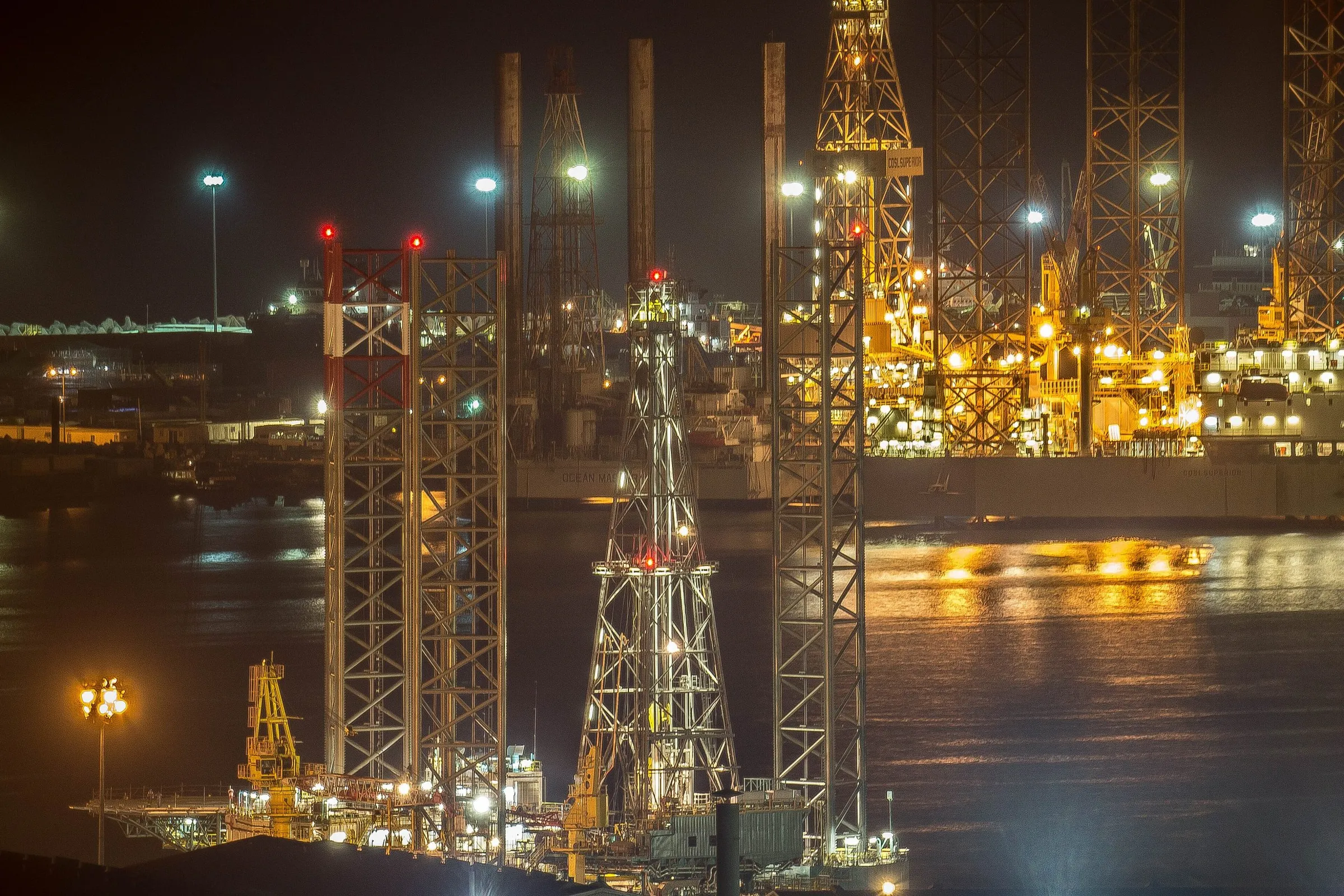 Ship repair yard lit at night on the water beside Dubai Maritime City, cranes and dry berths in use after dark