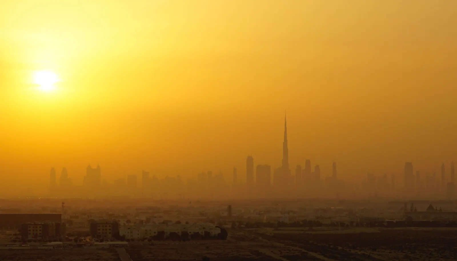 The Dubai skyline and Burj Khalifa silhouetted at dusk behind low-rise neighbourhoods