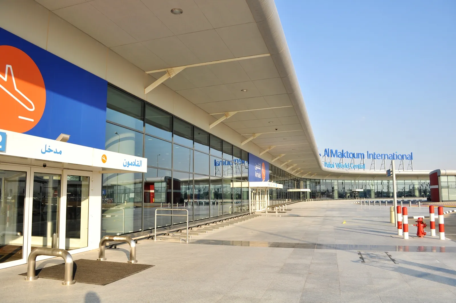The existing terminal frontage at Al Maktoum International Airport, Dubai South, with an empty forecourt and bilingual signage.