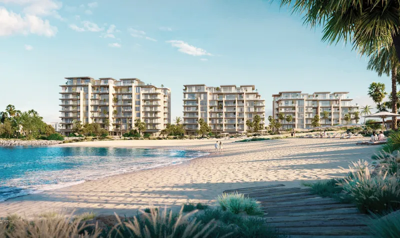 Three low rise Solaya buildings of pale stone and planted balconies seen across the sand of the private crescent beach at Jumeirah 1