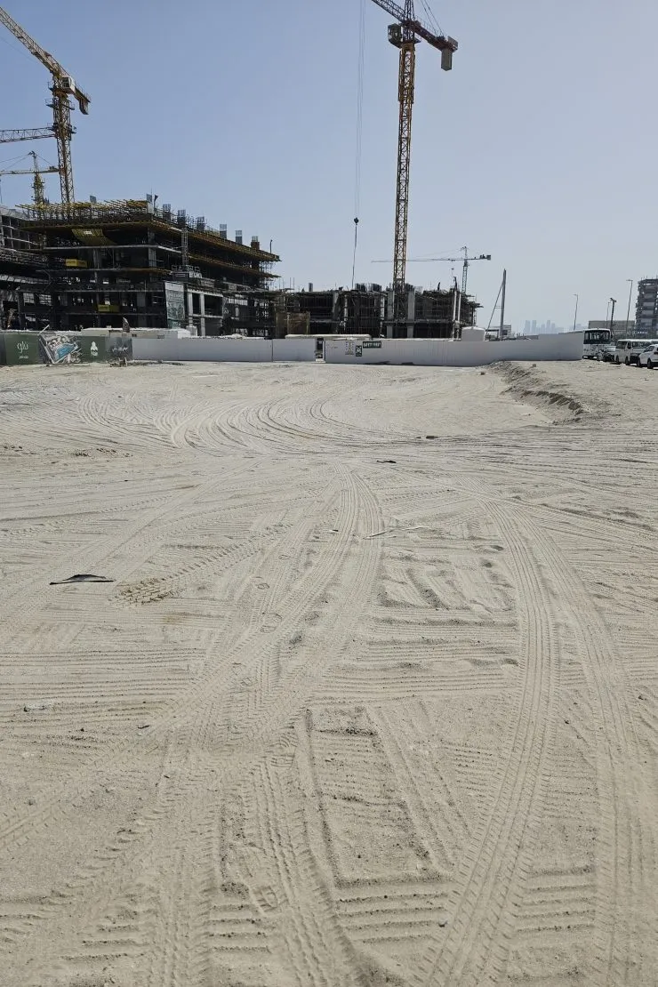 Cleared sand at the SOMA Residences plot on Dubai Islands with tower cranes over neighbouring construction