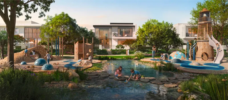 Render of the Talay childrens garden with a shallow stone-edged stream and stepping stones, a timber lighthouse play tower with slide, sand play mounds, and a detached villa with a walled garden behind