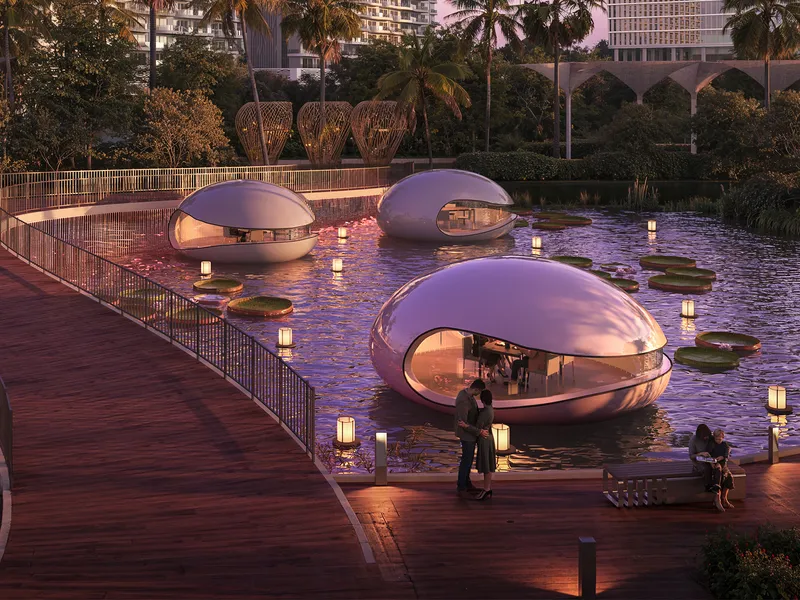 Glass-fronted floating pods on a lit pond beside a timber boardwalk at DAMAC Lagoons District