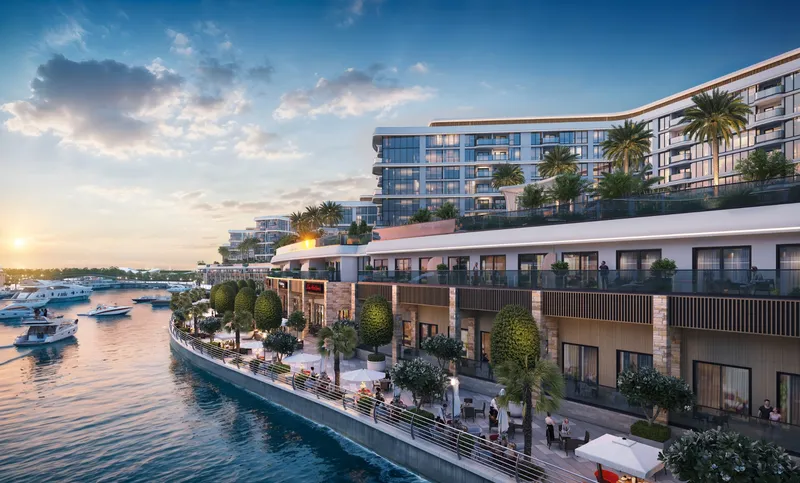 The marina promenade at dusk with restaurant terraces at the water's edge and apartments above