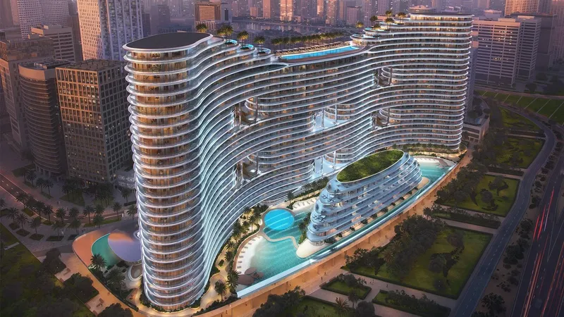 Aerial render of Binghatti Aquarise at dusk, showing the curved white balconies, podium pools and rooftop pool