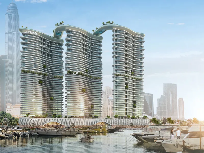 DAMAC Bay by Cavalli towers with a wave-shaped bridge at the crown, seen across the marina with yachts in the foreground
