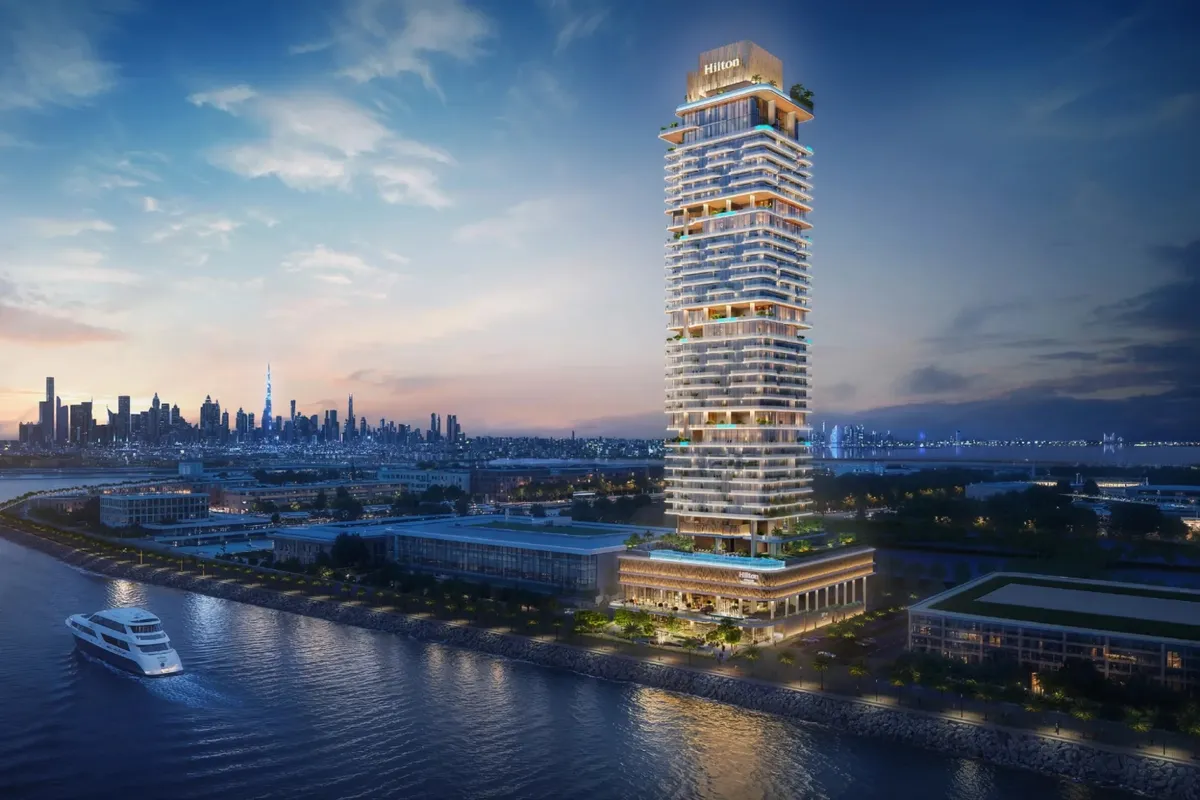 Evening render of the Hilton Residences tower on the Dubai Maritime City waterfront, with the Dubai skyline across the water