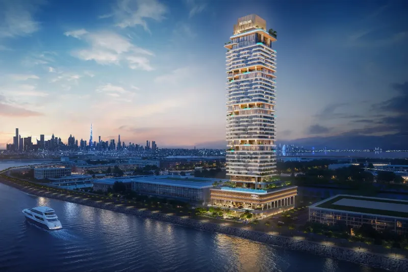 Evening render of the Hilton Residences tower on the Dubai Maritime City waterfront, with the Dubai skyline across the water