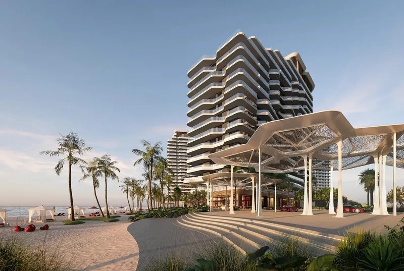 Rosso Bay Residences tower with curved white balconies behind the beach and a white canopy pavilion