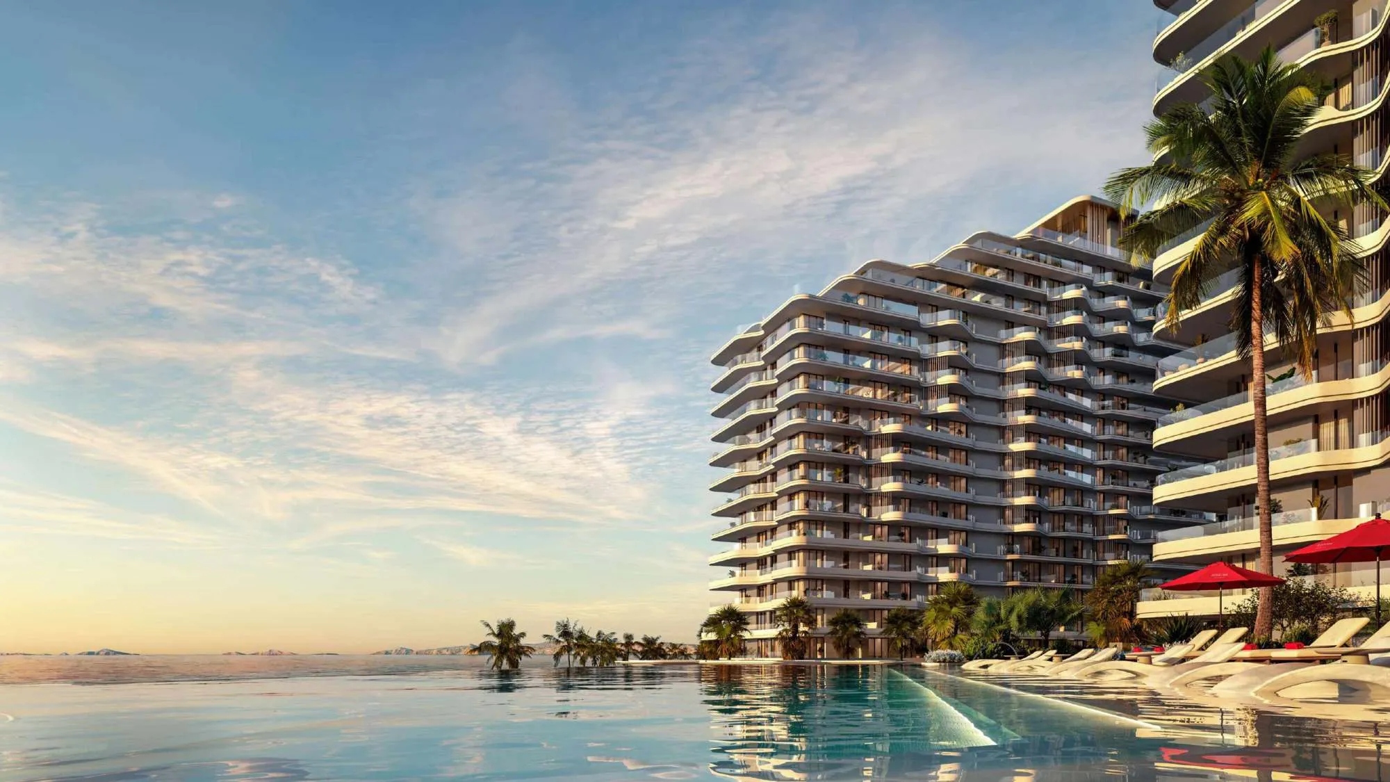 Rosso Bay Residences buildings with stepped balconies seen across the pool, with red parasols and palm trees