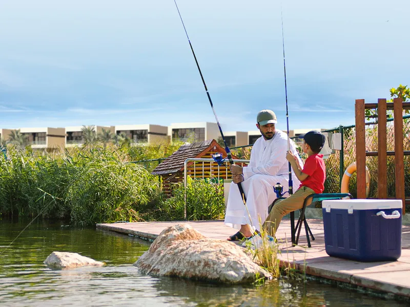 Father and son fishing from a deck on the lake in DAMAC Hills 2