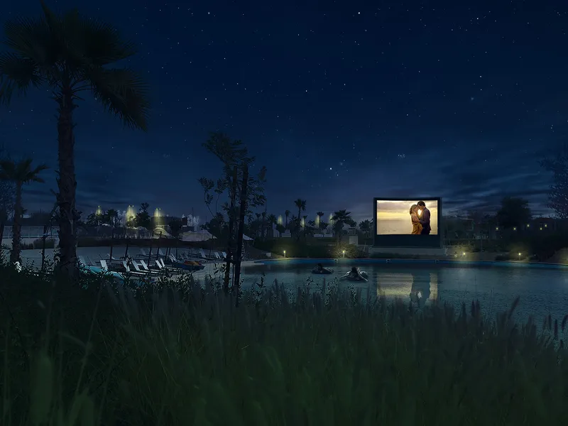 Outdoor cinema screen on the water at night with loungers on the shore in DAMAC Hills 2
